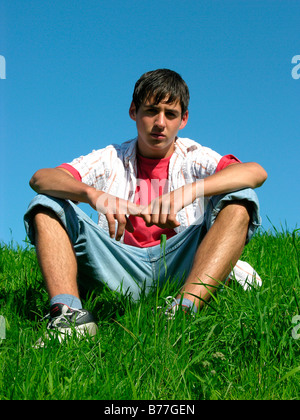 Ragazzo seduto su un prato in estate Foto Stock