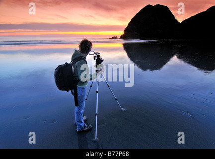 Camerawoman con filmato fotocamera riprese al tramonto con un treppiede a Meyers Creek Beach, pistola River State Park, Oregon Coast, Oregon Foto Stock