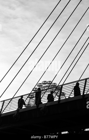 Pedoni stagliano contro London Eye passeggiando attraverso il Golden Jubilee passerella, Londra Foto Stock