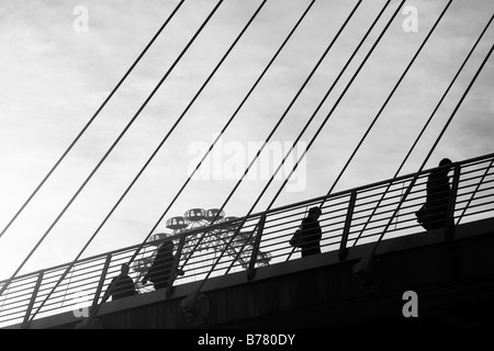 Pedoni stagliano contro London Eye passeggiando attraverso il Golden Jubilee passerella, Londra Foto Stock