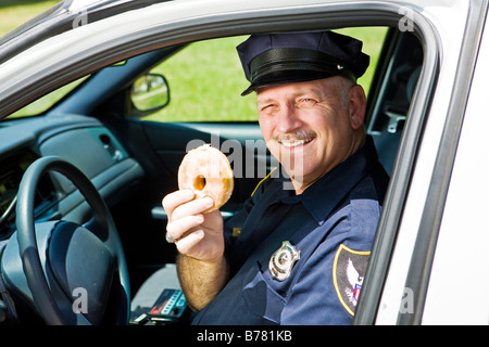 Funzionario di polizia nel suo squad car tenendo una ciambella Foto Stock