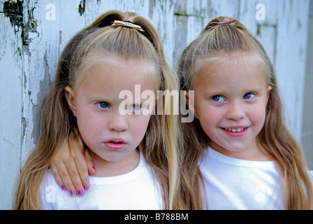 Twin quattro anni di ragazze che esprimono le emozioni contrastanti di felici e tristi,in piedi di fronte a un vecchio fienile bianco su una farm. Foto Stock