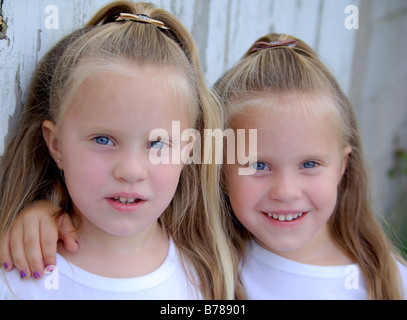 Twin quattro anni di ragazze cercando, sorridente ,in piedi accanto a un vecchio fienile nel paese. Foto Stock