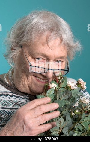 Il vecchio donna che indossa gli occhiali, fiori di contenimento Foto Stock