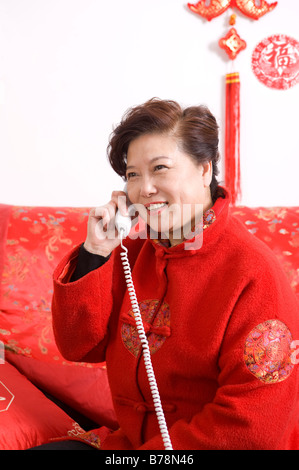 Donna anziana in abiti tradizionali e sorridente sul telefono Foto Stock