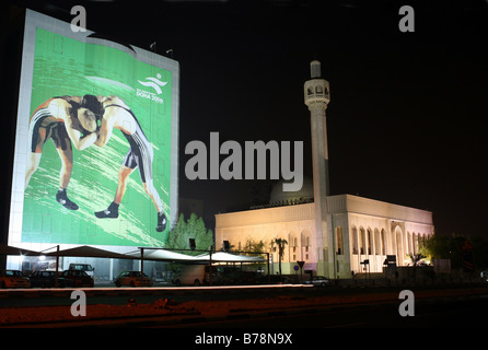 Un enorme poster pubblicitari di Doha Giochi Asiatici appeso su un edificio accanto alla Abu Bakr al Siddiqi moschea nel centro di Doha, in Qatar. Foto Stock