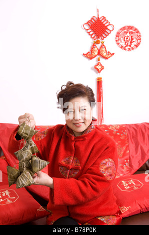 Donna anziana in abiti tradizionali azienda cinese gnocchi di riso e sorridente alla fotocamera Foto Stock