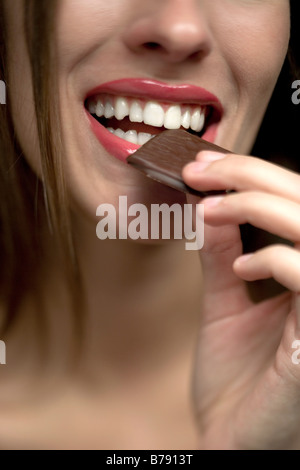 Giovane donna mettendo caramella di cioccolato a bocca, ritratto Foto Stock