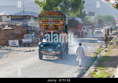 Ornati camion Pakistani auto e pedoni sulla strada principale di una piccola cittadina sulla Karakoram Highway in Pakistan Foto Stock