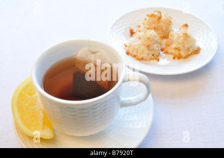 Una tazza di tè nero con limone e una piastra di amaretti di cocco su uno sfondo bianco. Foto Stock