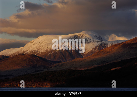 Il caloroso accesa coperta di neve vertice del Ben Nevis Scozia s montagna più alta aumenta al di sopra di colline scuro visto da di Ardgour Foto Stock