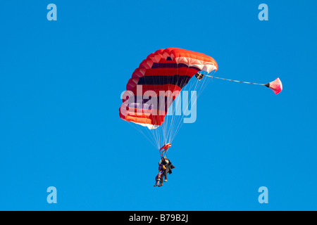 Paracadutismo TANDEM IN INGHILTERRA un rosso paracadute striato portante due persone scivola attraverso il cielo blu Foto Stock