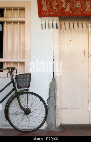 Bike con riporto cestello appoggiato contro una parete al di fuori di una casa in Georgetown, Penang, Malaysia Foto Stock