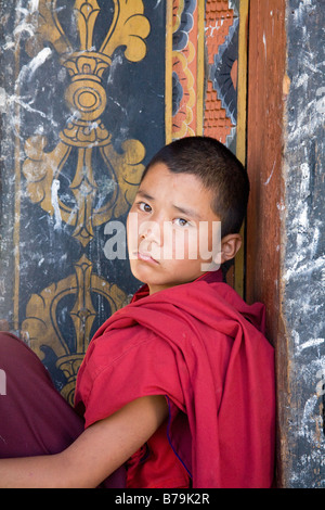 Un monaco novizio, con una triste guardare negli occhi, siede in una porta fuori Punaka Dzhong in Bhutan Foto Stock