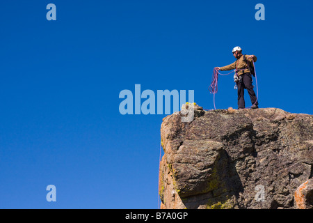 Un alpinista permanente sulla cima di una scogliera il suo avvolgimento fune di arrampicata Foto Stock