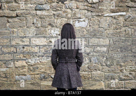 Giovane donna rivolta verso il muro di pietra Foto Stock