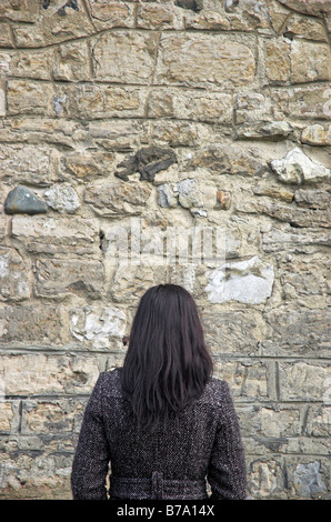 Giovane donna rivolta verso il muro di pietra Foto Stock