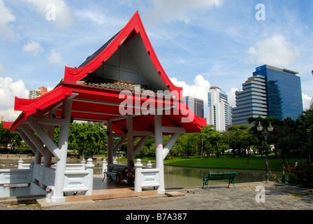 Piccolo tempio con un tetto rosso nella parte anteriore dei moderni edifici multipiano, Queens Park, Bangkok, Thailandia, Sud-est asiatico Foto Stock