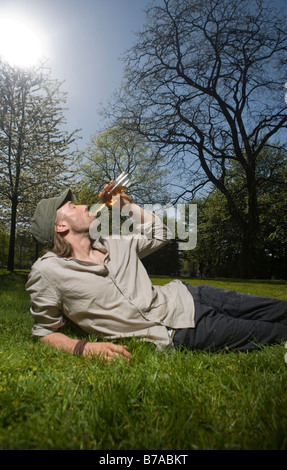 Giovane uomo seduto in un parco, bere Foto Stock