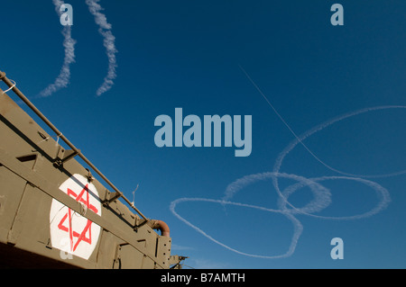 Il fumo proveniente da getti israeliano lasciano scie nel cielo con APC corazzato portatori di personale presso la frontiera israeliana con la striscia di Gaza Foto Stock