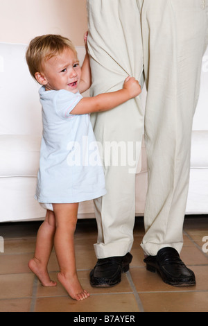 Bambino piange, afferrando papà della gamba Foto Stock