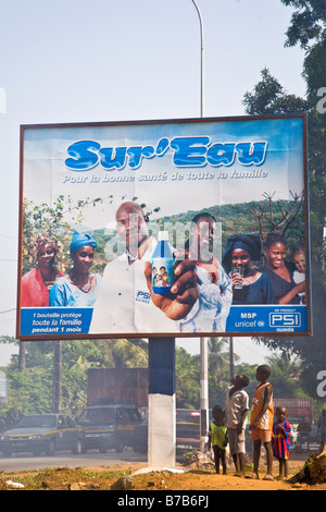 I bambini guardano fino a una pubblicità tramite Affissioni Sur Eau su una strada trafficata attraverso la Guinea la capitale Conakry. Foto Stock