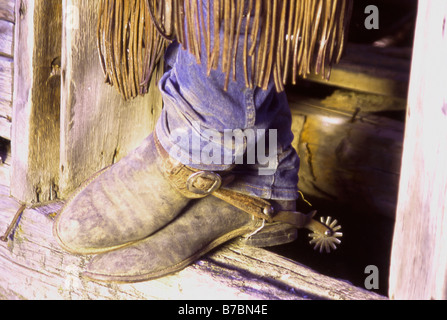 Un cowboy s rotto nella vecchia e fidata stivali alla porta di un vecchio log cabin in un ranch in gli Stati Uniti occidentali Foto Stock