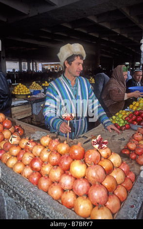 Uomo in cappello di pelliccia vendita di melograni e mele Kolhoznaya bazaar coperto Samarcanda Uzbekistan Asia il bazar è premuto contro Foto Stock