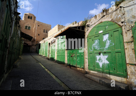 Scena di strada a Hebron sotto occupazione israeliana: graffitis di David Star mettere da coloni ebrei su chiuso negozi arabi. Foto Stock