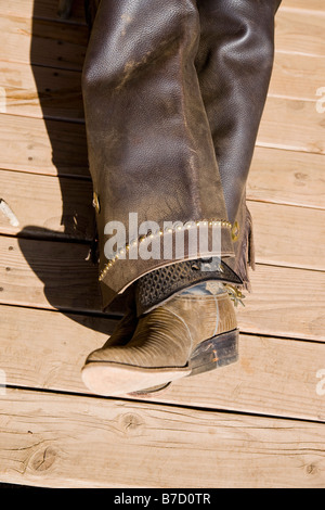 Stivali in pelle e chaps di un cowboy giacente su di un pavimento in legno Foto Stock