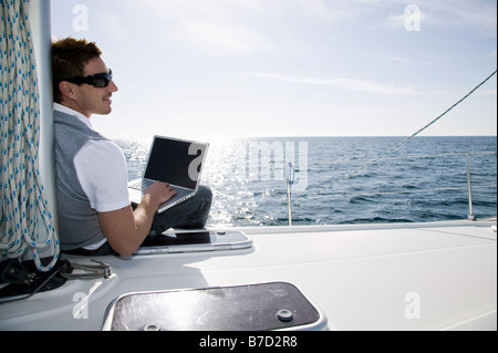 Vista posteriore di un uomo che utilizza un computer portatile su un yacht Foto Stock