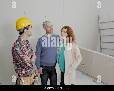 Un imprenditore edile parlando con una giovane coppia in un sito di costruzione Foto Stock