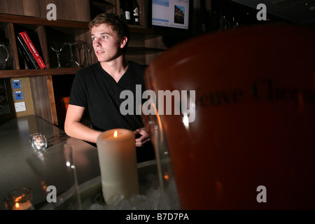 Ritratto di un giovane maschio attraente barista tirando una pinta di birra in un bar alla moda di Londra. Egli è sempre sorridente e guardando la telecamera Foto Stock