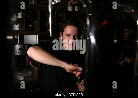 Ritratto di un giovane maschio attraente barista tirando una pinta di birra in un bar alla moda di Londra. Egli è sempre sorridente e guardando la telecamera Foto Stock