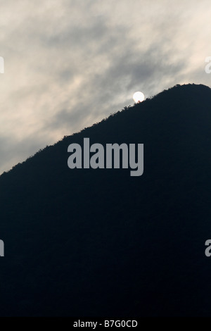 Sole che tramonta dietro il picco di montagna Foto Stock