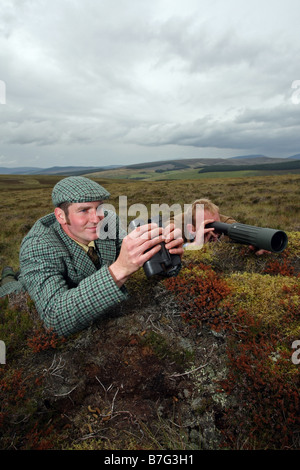 Stalker usando il binocolo e telescopio al posto di cervi sulle colline in Scozia, Regno Unito Foto Stock