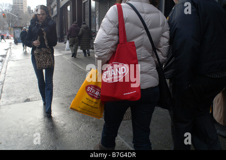 Una donna cammina giù Broadway a New York al quartiere della East Village portando un filamento bookstore tote Foto Stock