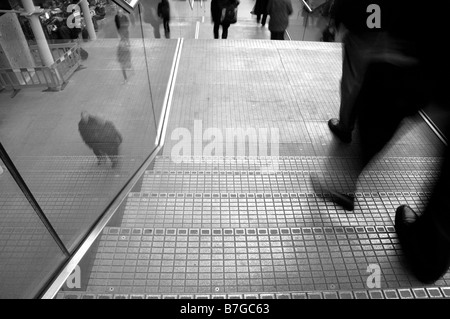 Immagine in bianco e nero di un uomo per le gambe e piedi giù per le scale in movimento sfocate con la gente che camminava sul marciapiede di seguito. Foto Stock