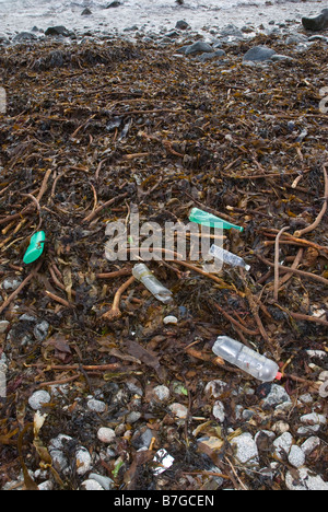 Varie bottiglie di plastica e contenitori lavati fino a una coperta di alghe marine beach. Foto Stock