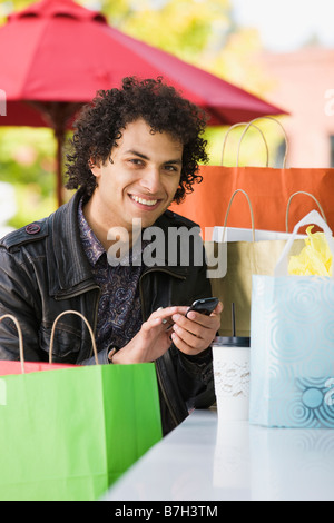 Medio Orientale con uomo borse per lo shopping di messaggistica di testo sul telefono cellulare Foto Stock