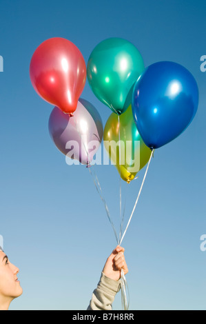 Chiudere verticale fino a una giovane ragazza adolescente tenendo un mazzetto colorato e riempito di elio Palloncini di lattice contro un cielo blu Foto Stock