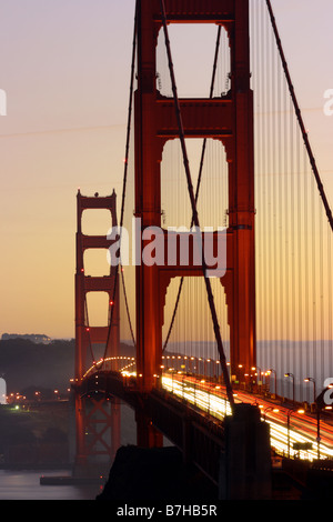 Fari di traffico di creare percorsi di luce sul Golden Gate Bridge in arancione tramonto. San Francisco California USA Foto Stock