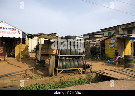 Una donna e un cane sedersi all'ombra su strada la vendita di seconda mano pneumatici e verdure Foto Stock