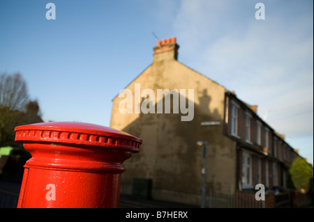 La parte superiore di un montante rosso postbox con un ombra di un tetto sul retro Foto Stock