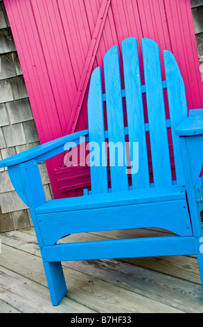 Una luminosa sala Blu beach sedia in legno, su un portico con una rosa caldo o porta magenta, d'estate. Foto Stock