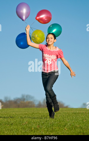 Ritratto verticale di una giovane ragazza che corre sotto il sole con un mucchio di palloncini luminosi Foto Stock