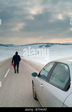 L'uomo inizia il lungo percorso a piedi in un paese isolato strada in inverno per trovare il carburante per il suo ripartiti in auto Foto Stock