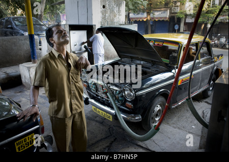 Un taxi cab driver orologi il prezzo sul riempimento pompa la sua cabina con gas naturale compresso in Mumbai, India. Foto Stock