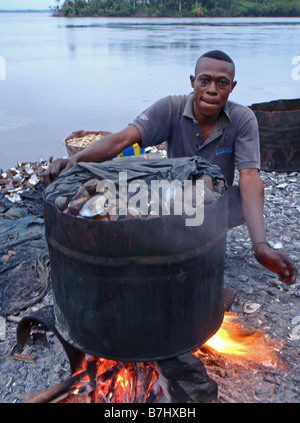 Fisherman ebollizione cozze vongole ostriche pesce a guscio in metallo grande tamburo di ferro sulle rive del fiume Congo Repubblica Democratica del Congo Foto Stock