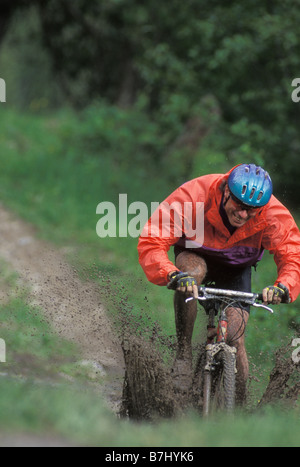 Giovane uomo mountain bike attraverso il fango vicino al Fernie, BC, Canada Foto Stock